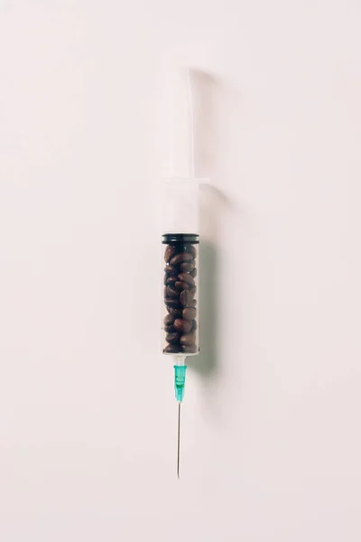 Top view of syringe filled with coffee beans on white surface — Stock Photo