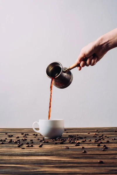 Cropped shot of woman pouring coffee into cup from cezve on rustic wooden table — Stock Photo