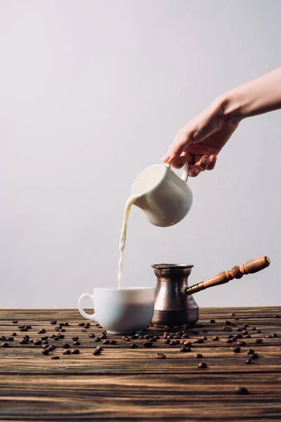 Cropped shot of woman pouring milk into coffee on rustic wooden table — Stock Photo