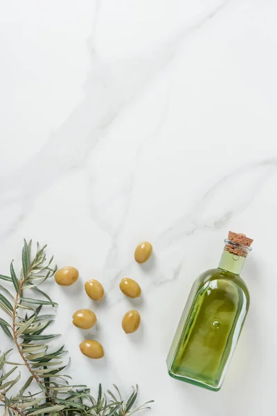 Draufsicht auf eine Flasche Olivenöl, Zweige und Oliven auf einem Marmortisch — Stockfoto