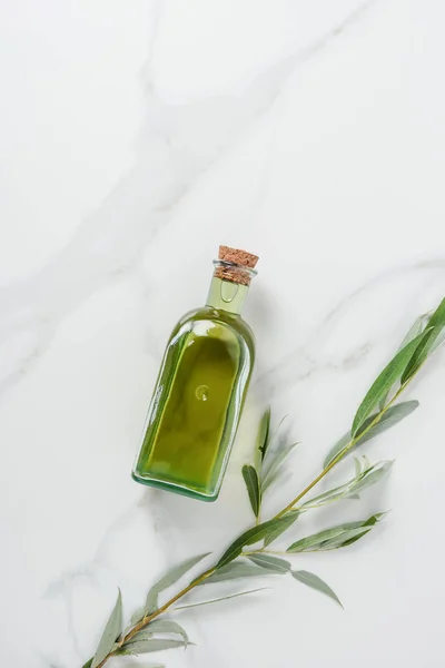 Draufsicht auf eine Flasche Olivenöl und Zweige auf einem Marmortisch — Stockfoto