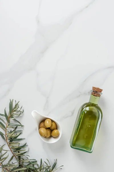 Vista dall'alto di bottiglia di olio d'oliva e olive in ciotola su superficie marmorea — Foto stock