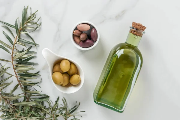 Blick von oben auf Olivenöl und leckere Oliven in Schalen auf Marmoroberfläche — Stockfoto