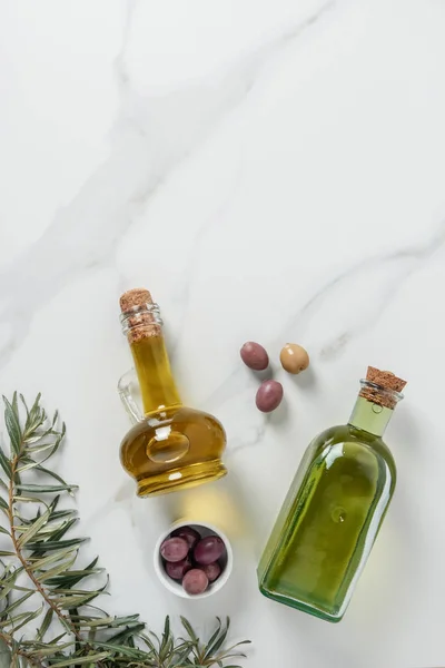 Top view of olive oil in glass bottles and olives on marble table — Stock Photo