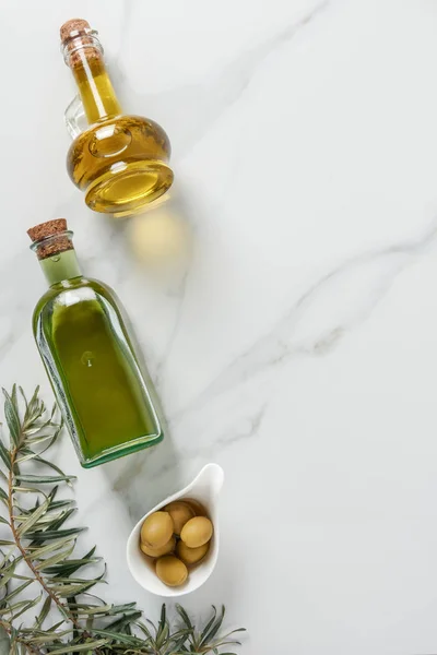 Vista dall'alto dell'olio d'oliva in bottiglie di vetro e olive su piano in marmo — Foto stock