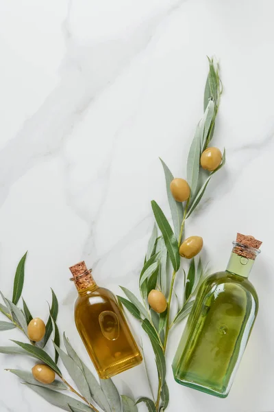 Top view of bottles of olive oil and twigs with olives on marble table — Stock Photo