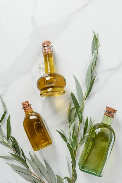 Top view of bottles of three bottles of olive oil and twigs on marble table — Stock Photo