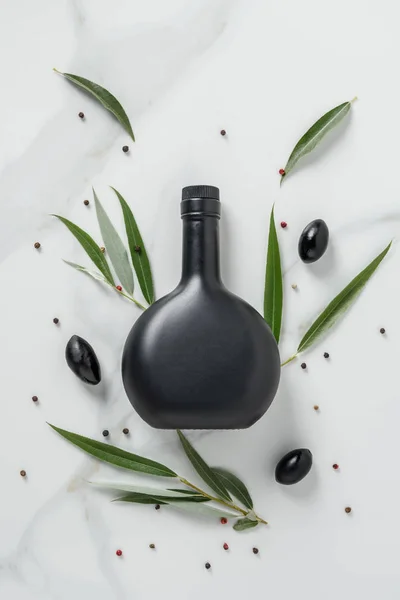 Top view of black bottle of olive oil and olives on marble table — Stock Photo