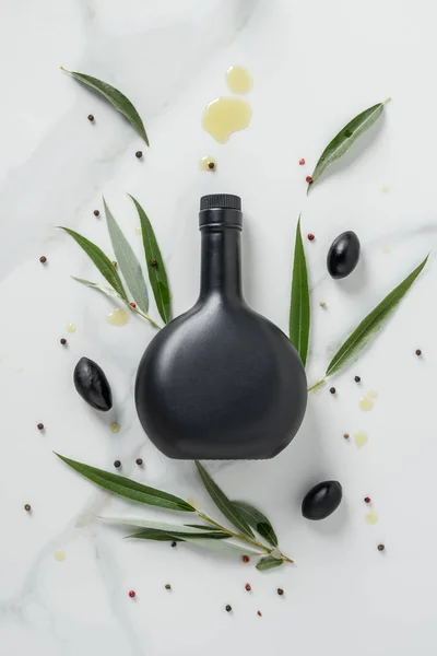 Підвищений вид на чорну пляшку оливкової олії та оливок на мармуровому столі — стокове фото