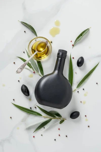 Draufsicht auf schwarze Flasche Olivenöl und Glas mit Löffel auf Marmortisch — Stockfoto