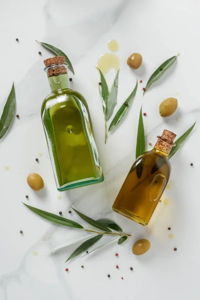 Vista superior de dos botellas de aceite de oliva y ramitas sobre mesa de mármol - foto de stock