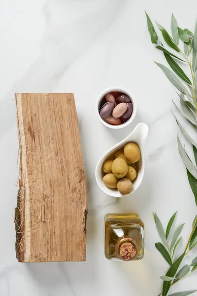 Elevated view of bottle of olive oil, log and olives in bowls on marble table — Stock Photo