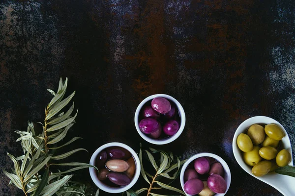 Blick auf verschiedene Oliven für Olivenöl und Zweige auf schäbiger Oberfläche — Stockfoto