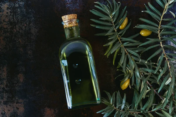 Верхний вид бутылки вкусного оливкового масла, веток и оливок на потрепанной поверхности — стоковое фото