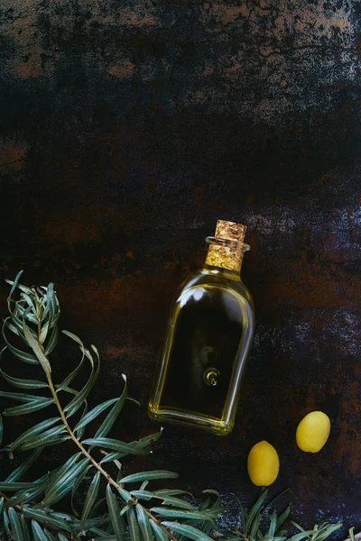 Vista elevada de la botella de aceite de oliva, ramitas y aceitunas apetitosas en la superficie de mala calidad - foto de stock
