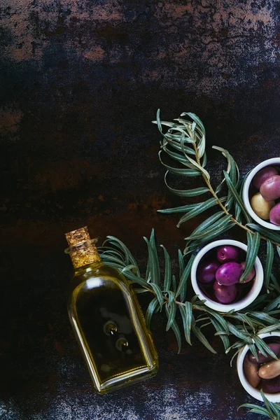 Vista elevada de diferentes aceitunas deliciosas y botella de aceite en la superficie de mala calidad - foto de stock