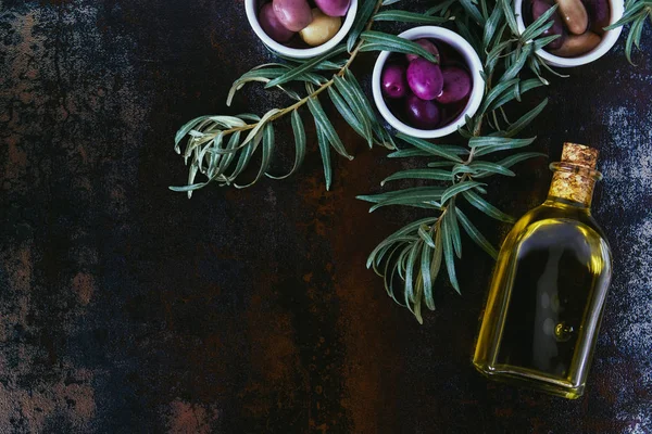 Вид сверху на различные оливки и бутылку масла на потрепанной поверхности — стоковое фото