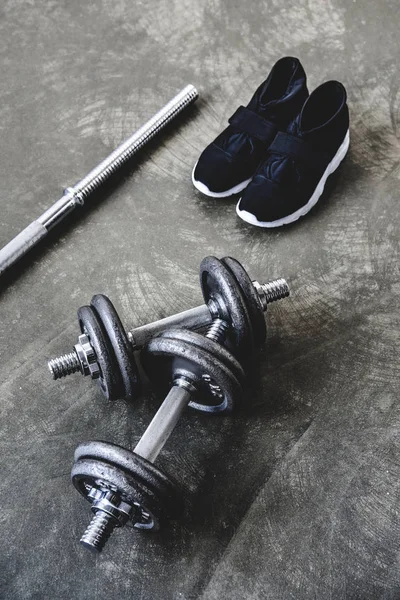 Top view of adjustable dumbbells and bar with sneakers on concrete surface — Stock Photo