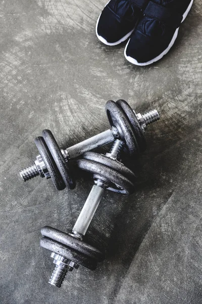 Top view of adjustable dumbbells with sneakers on concrete surface — Stock Photo