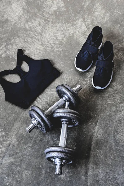 High angle view of dumbbells with sneakers and sport bra on concrete surface — Stock Photo