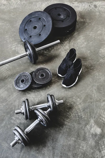 Dumbbells and barbell with weight plates and sneakers on grungy grey floor — Stock Photo