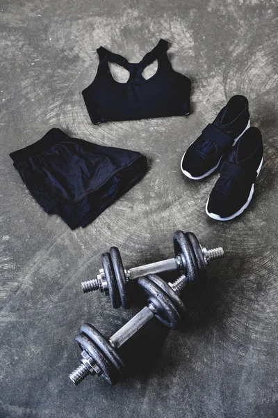 High angle view of dumbbells with sneakers and female sportswear on concrete surface — Stock Photo