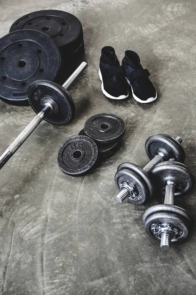 Vista de ángulo alto de varios equipos de gimnasio y zapatillas de deporte en el suelo de hormigón - foto de stock