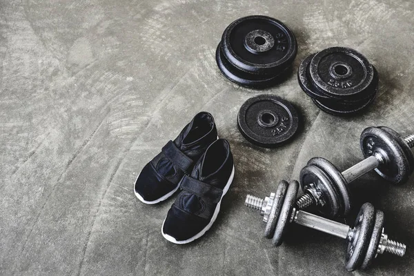 Vista ad alto angolo di manubri con dischi e scarpe da ginnastica sul pavimento di cemento — Foto stock