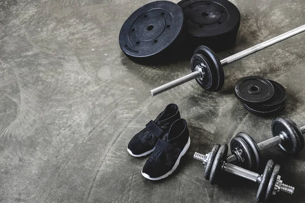 Dumbbells and barbell with weight plates and sneakers on concrete floor — Stock Photo