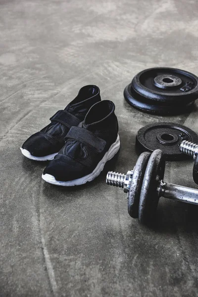 Close-up shot of dumbbells with weight plates and sneakers on concrete floor — Stock Photo