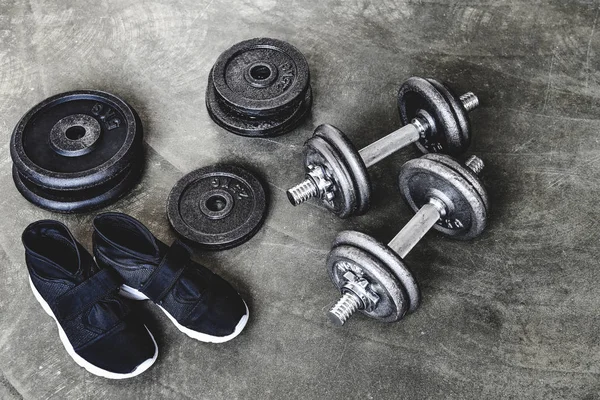 Primer plano de mancuernas con placas de peso y zapatillas de deporte en la superficie de hormigón - foto de stock