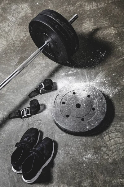 Sneakers with wrist wraps and barbell on concrete surface — Stock Photo