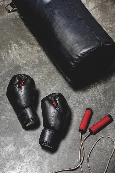 Saco de boxeo con cuerda de salto y guantes de boxeo en superficie de hormigón - foto de stock