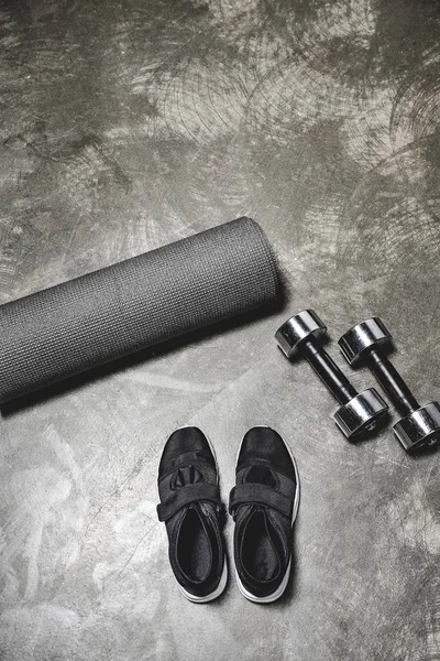 Vista dall'alto di scarpe da ginnastica con tappetino yoga e manubri sdraiati su una superficie di cemento — Foto stock