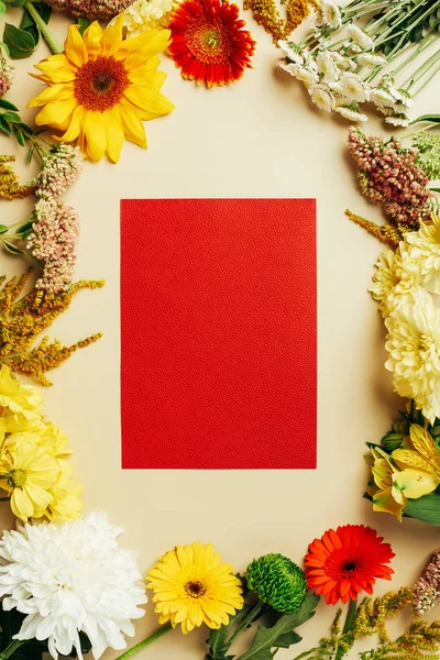 Flat lay with various beautiful flowers and blank red card on beige background — Stock Photo