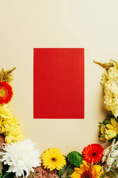 Flat lay com várias flores bonitas e cartão vermelho em branco no fundo bege — Fotografia de Stock