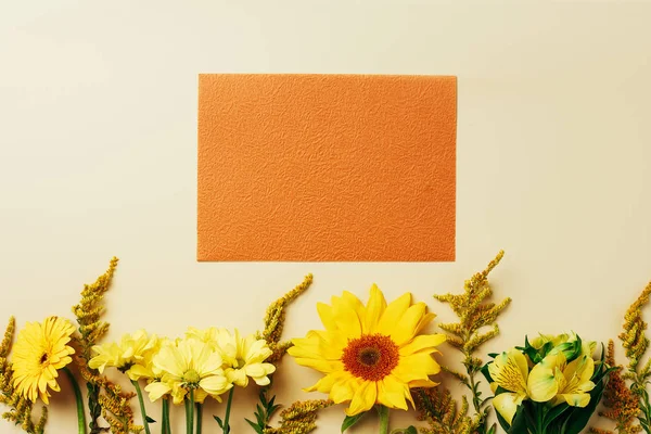 Flat lay with beautiful flowers and empty orange card arrangement on beige backdrop — Stock Photo