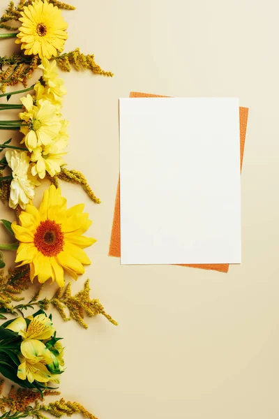 Flat lay com flores brilhantes, branco vazio e cartões laranja sobre fundo bege — Fotografia de Stock