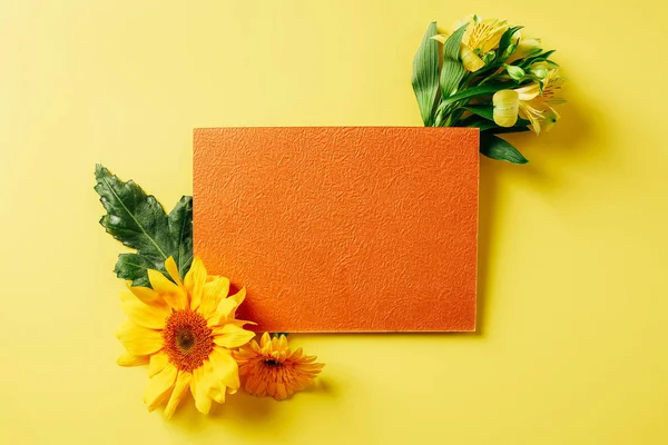 Вид сверху на пустую оранжевую открытку, подсолнух, герберу и цветы лилии на желтом фоне — стоковое фото