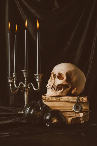 Halloween skull on ancient books with black pumpkin, apple and candles on black cloth — Stock Photo