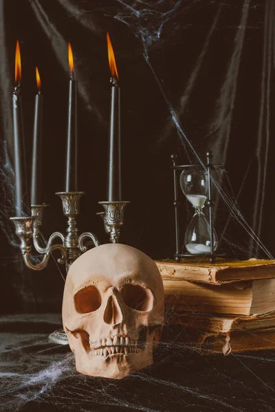 Cráneo de Halloween, libros antiguos con reloj de arena y velas en tela negra - foto de stock