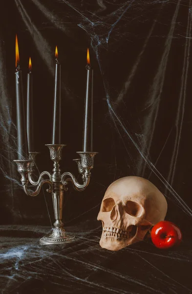 Calavera, manzana roja y candelabro con velas sobre tela negra con tela de araña - foto de stock