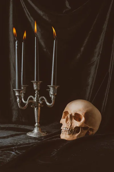 Crâne effrayant et candélabre avec des bougies noires sur un tissu sombre pour Halloween — Photo de stock