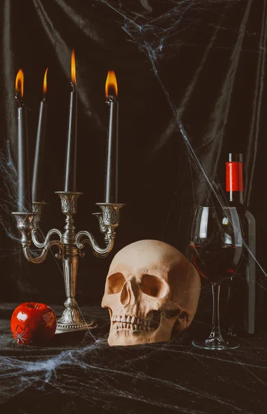 Halloween Totenkopf, Apfel, Rotwein und Kandelaber mit Kerzen auf schwarzem Tuch mit Spinnennetz — Stockfoto