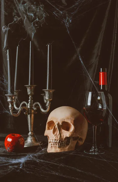 Calavera, manzana, vino tinto y candelabro con velas ahumadas sobre tela negra con tela de araña - foto de stock