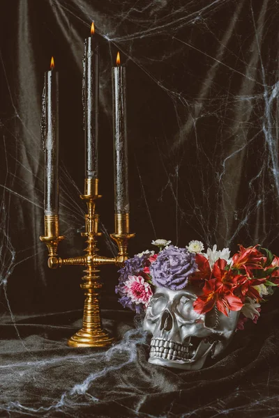 Silver skull with flowers and candelabrum with candles on black cloth with spider web for halloween — Stock Photo