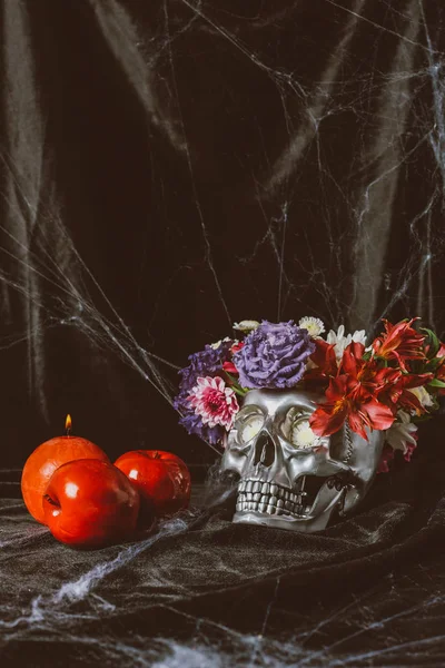 Silberner Totenkopf mit Blumen, Kerze und Äpfeln auf schwarzem Tuch mit Spinnennetz — Stockfoto