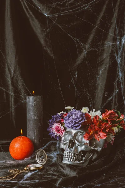 Silberner Halloween-Totenkopf mit Blumen, Vintage-Uhr und Kerzen auf schwarzem Tuch mit Spinnennetz — Stockfoto