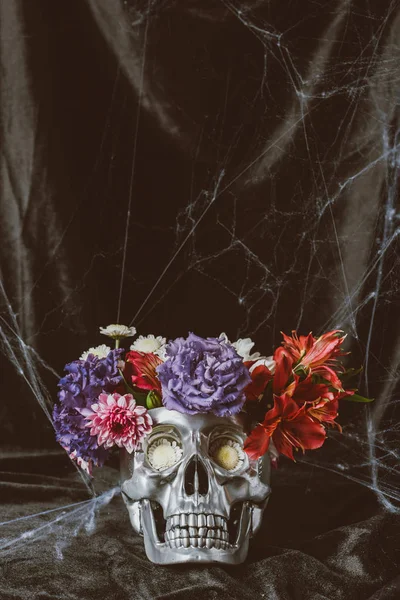 Cráneo de halloween plateado con flores en tela oscura con tela de araña - foto de stock