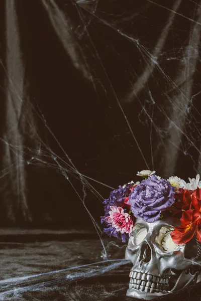 Silver skull with flowers on black cloth with spider web — Stock Photo